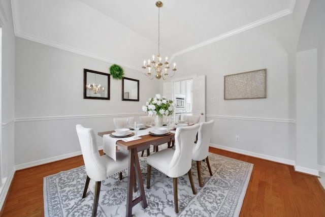 dining space featuring lofted ceiling, baseboards, a chandelier, and wood finished floors