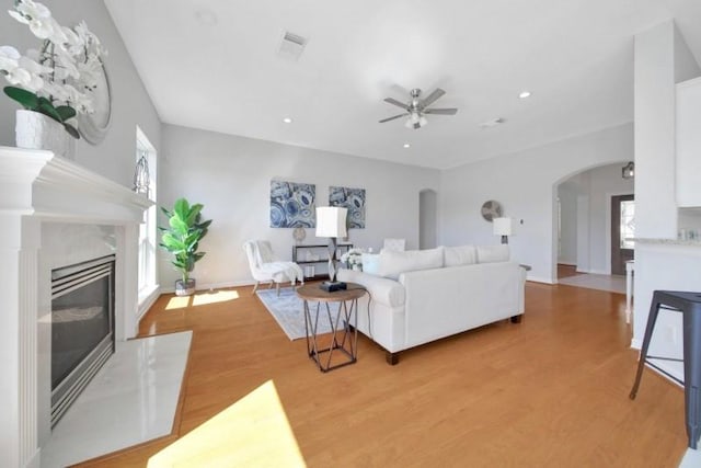 living area featuring arched walkways, a premium fireplace, a ceiling fan, visible vents, and light wood-style floors