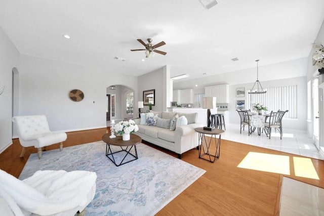 living area with arched walkways, recessed lighting, ceiling fan with notable chandelier, visible vents, and light wood-style floors