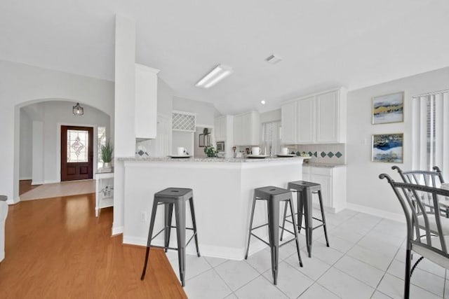 kitchen with arched walkways, a peninsula, a kitchen breakfast bar, vaulted ceiling, and tasteful backsplash