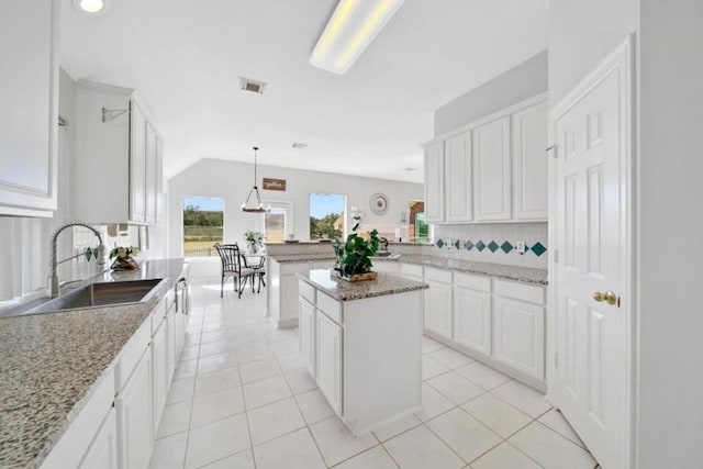 kitchen with light tile patterned floors, backsplash, white cabinets, vaulted ceiling, and a sink