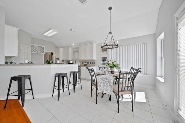 dining area with lofted ceiling, light tile patterned floors, baseboards, and a notable chandelier