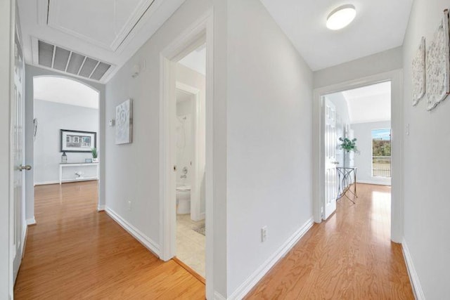 hallway featuring arched walkways, light wood-style flooring, visible vents, baseboards, and attic access