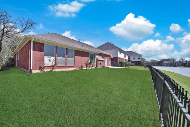 back of property with a fenced backyard, a lawn, brick siding, and a water view