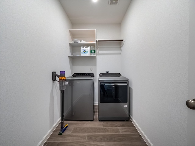 clothes washing area featuring visible vents, baseboards, wood finish floors, laundry area, and washer and dryer