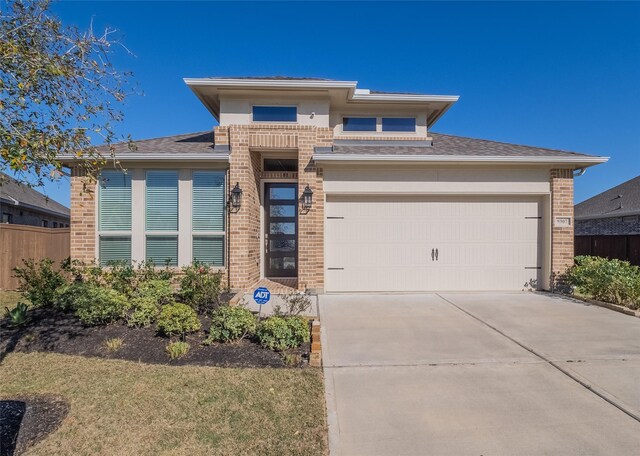 prairie-style home featuring brick siding, an attached garage, concrete driveway, and fence