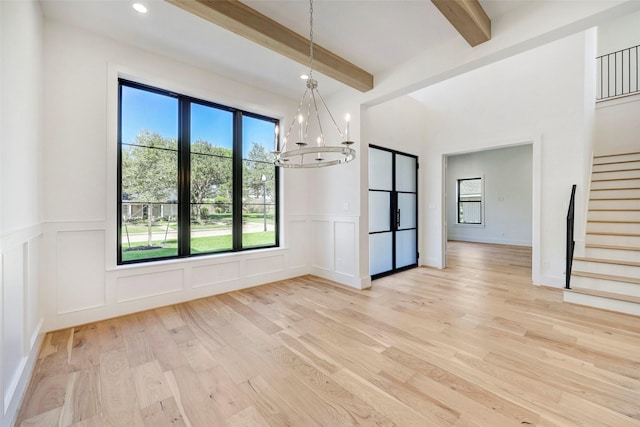 unfurnished dining area with stairway, light wood-style floors, a decorative wall, beamed ceiling, and a notable chandelier