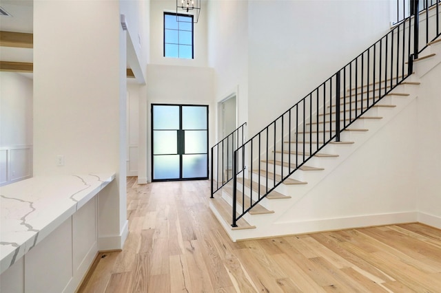 entrance foyer with stairway, baseboards, visible vents, light wood-style flooring, and a towering ceiling