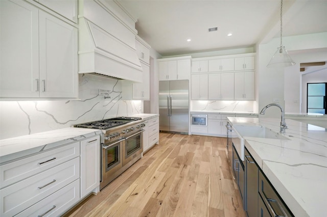 kitchen with white cabinets, high end appliances, premium range hood, and light wood-type flooring