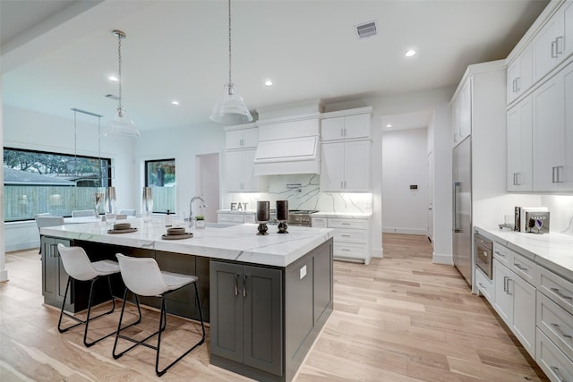 kitchen featuring built in appliances, decorative backsplash, light wood-style flooring, a large island, and white cabinetry