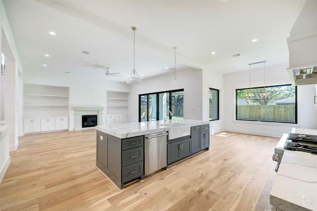 kitchen with light stone counters, a ceiling fan, a sink, stainless steel dishwasher, and light wood-type flooring