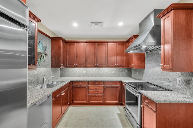 kitchen with light stone counters, a sink, decorative backsplash, appliances with stainless steel finishes, and wall chimney exhaust hood