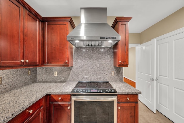 kitchen featuring tasteful backsplash, light stone counters, stainless steel electric range, and wall chimney range hood