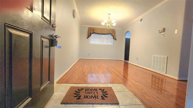 foyer entrance featuring crown molding, visible vents, a textured ceiling, wood finished floors, and a chandelier