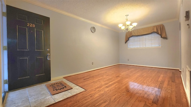 entrance foyer featuring light wood-style floors, a notable chandelier, a textured ceiling, and ornamental molding