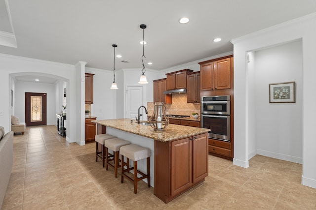 kitchen with a breakfast bar area, light stone counters, arched walkways, appliances with stainless steel finishes, and backsplash