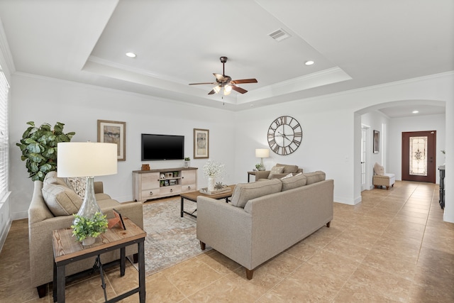 living area featuring arched walkways, visible vents, a ceiling fan, and a tray ceiling