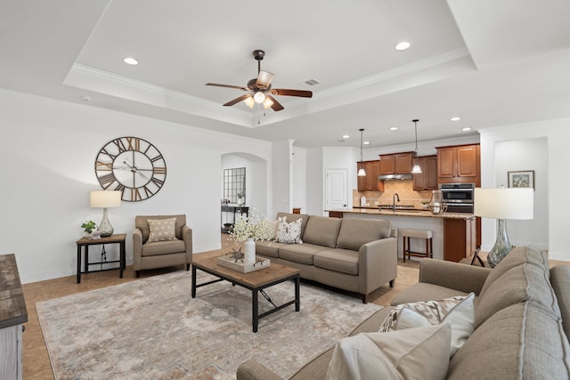 living area with a tray ceiling, ornamental molding, arched walkways, and ceiling fan