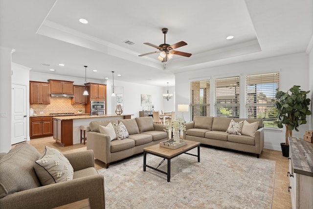 living room with a raised ceiling, crown molding, ceiling fan with notable chandelier, and visible vents