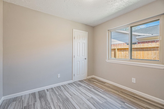 spare room featuring a textured ceiling, baseboards, and wood finished floors