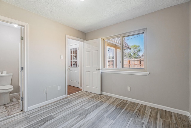 unfurnished bedroom with ensuite bath, wood finished floors, baseboards, and a textured ceiling