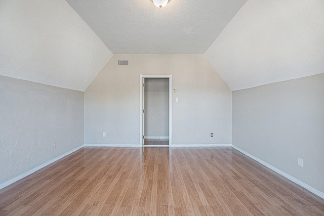 bonus room featuring visible vents, a textured ceiling, baseboards, light wood finished floors, and lofted ceiling