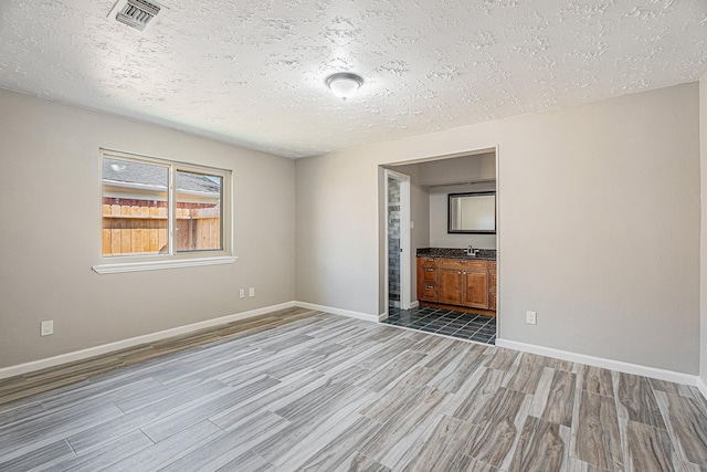 empty room with baseboards, visible vents, a sink, a textured ceiling, and light wood-type flooring
