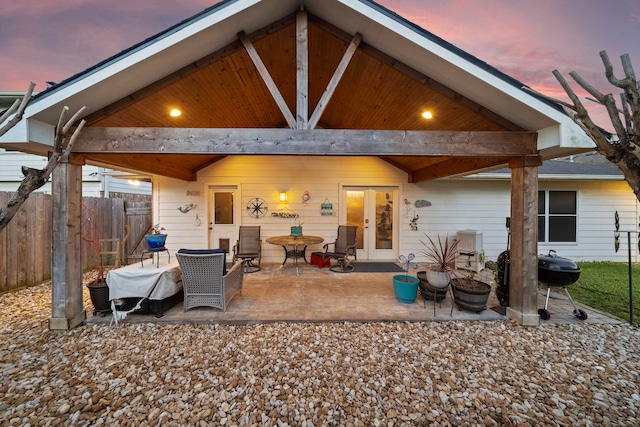 back of property at dusk with french doors, a patio area, and fence