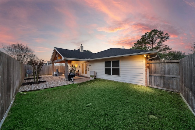 back of house at dusk with a chimney, a patio area, a yard, and a fenced backyard