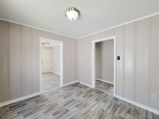 spare room with ornamental molding, a decorative wall, light wood-style flooring, and baseboards