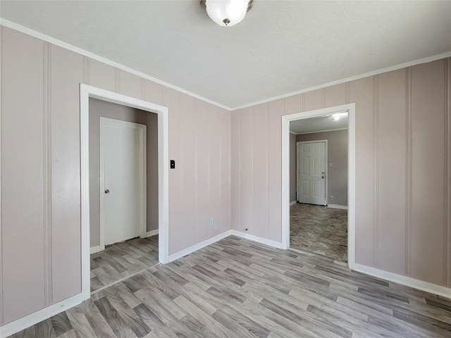 unfurnished room with light wood finished floors, baseboards, a decorative wall, and crown molding