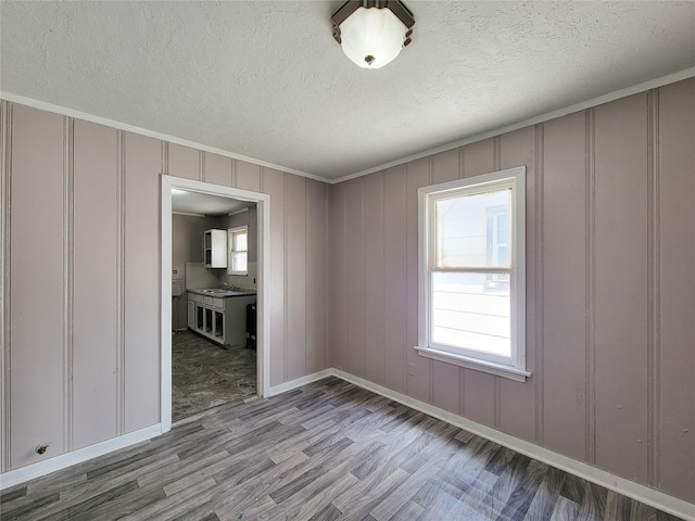 unfurnished room featuring crown molding, a sink, a textured ceiling, wood finished floors, and baseboards