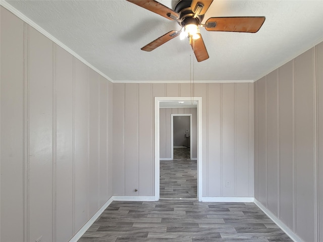 spare room with crown molding, a textured ceiling, baseboards, and wood finished floors