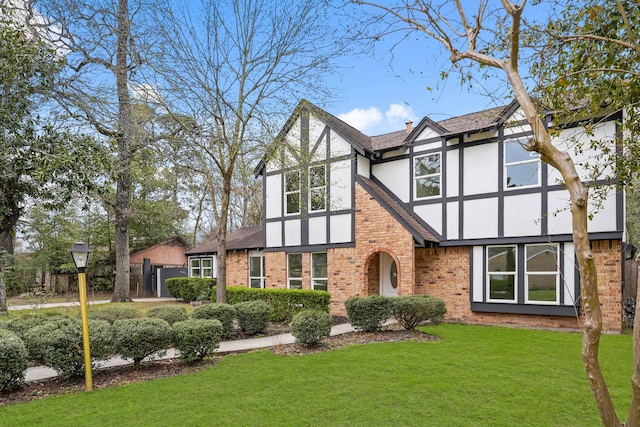 tudor house featuring brick siding, fence, roof with shingles, stucco siding, and a front yard