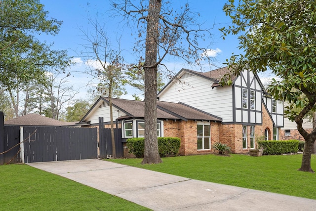 view of front of property featuring brick siding, a shingled roof, fence, driveway, and a front lawn