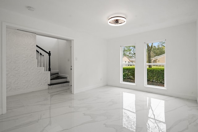 empty room featuring marble finish floor, baseboards, and stairs