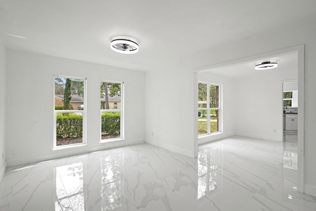 unfurnished room with marble finish floor, a healthy amount of sunlight, and baseboards