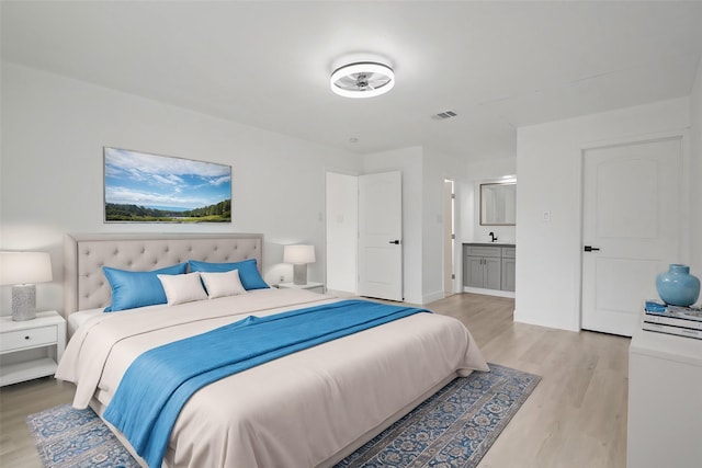 bedroom with connected bathroom, light wood-type flooring, visible vents, and a sink