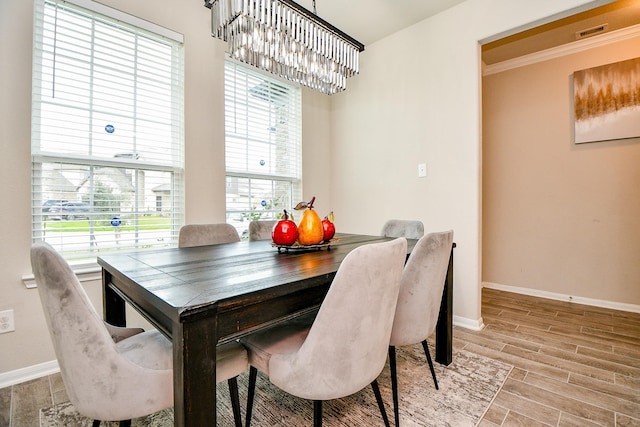 dining space with wood finish floors, visible vents, baseboards, ornamental molding, and an inviting chandelier