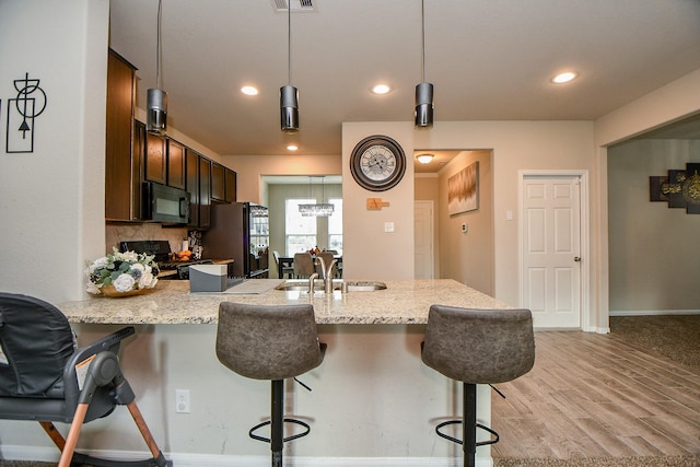 kitchen featuring light stone counters, a breakfast bar area, a peninsula, light wood-type flooring, and black appliances