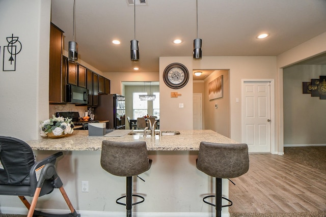 kitchen featuring a peninsula, a kitchen breakfast bar, black appliances, light wood-type flooring, and light stone countertops