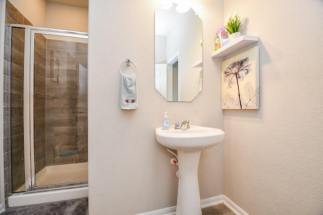 bathroom featuring baseboards, a stall shower, and a sink