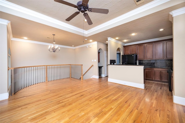 kitchen with dark countertops, arched walkways, freestanding refrigerator, a raised ceiling, and light wood-type flooring