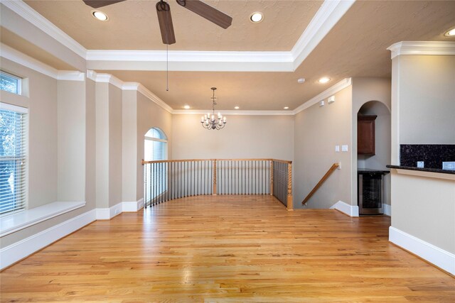 spare room with light wood finished floors, wine cooler, a tray ceiling, ornamental molding, and recessed lighting