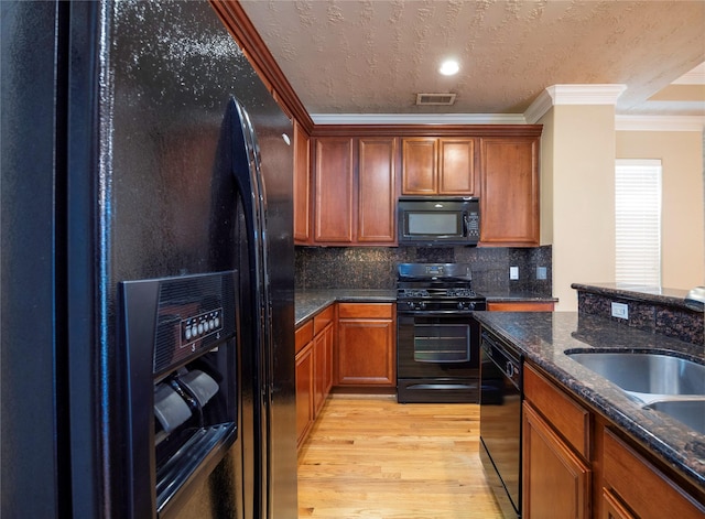 kitchen featuring visible vents, black appliances, light wood-style floors, crown molding, and backsplash