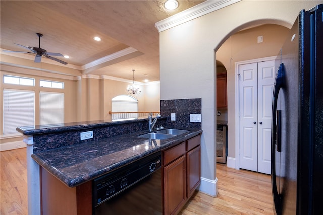 kitchen with light wood-style floors, arched walkways, black appliances, a raised ceiling, and a sink