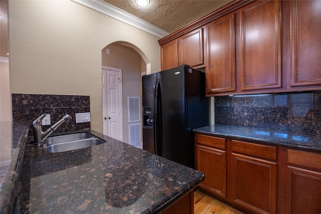 kitchen with tasteful backsplash, crown molding, arched walkways, black fridge with ice dispenser, and a sink