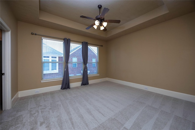 carpeted spare room featuring a tray ceiling, baseboards, and ceiling fan