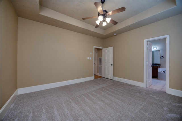 unfurnished bedroom with baseboards, a tray ceiling, ensuite bathroom, a textured ceiling, and light colored carpet