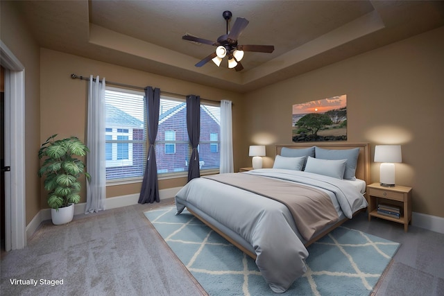 carpeted bedroom featuring a ceiling fan, a raised ceiling, and baseboards